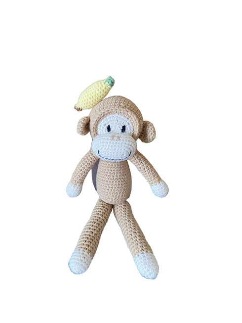 Crocheted monkey toy with a banana on a wooden surface